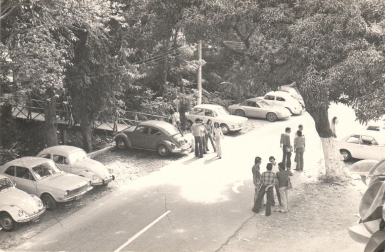 Vista da via de passagem principal da PUC-Rio e da primeira ponte de acesso ao Edifício da Amizade, com alunos e carros. 1980. Fotógrafo Antônio Albuquerque. Acervo da Vice-Reitoria de Desenvolvimento.