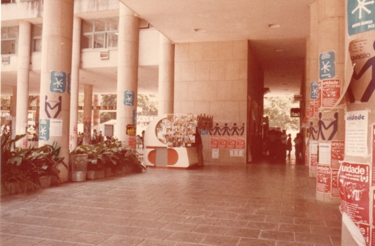 Na entrada da Ala Frings, paredes cobertas com propagandas do movimento estudantil na PUC-Rio. Ao centro a banca de jornal que ficava onde atualmente há um caixa eletrônico. 1985. Fotógrafo desconhecido. Acervo do Projeto Comunicar.