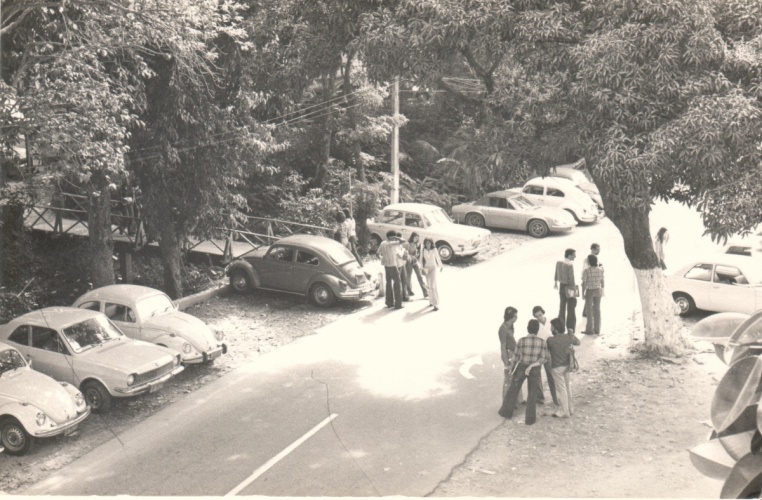 Vista da via de passagem principal da PUC-Rio e da primeira ponte de acesso ao Edifício da Amizade, com alunos e carros. 1980. Fotógrafo Antônio Albuquerque. Acervo da Vice-Reitoria de Desenvolvimento. Vista da via de passagem principal da PUC-Rio e da primeira ponte de acesso ao Edifício da Amizade, com alunos e carros. 1980. Fotógrafo Antônio Albuquerque. Acervo da Vice-Reitoria de Desenvolvimento.