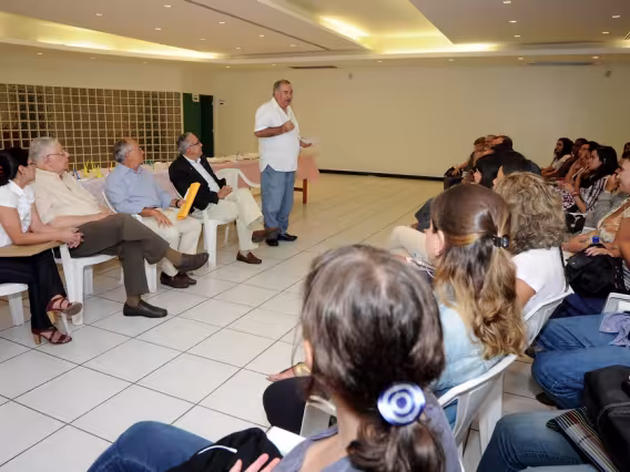 No Salão da Pastoral, sentados, Rita Luquini, Prof. Fernando Ferreira, Prof. Augusto Sampaio e o Reitor Prof. Pe. Josafá S.J., e, de pé, o Prof. Miguel Pereira. Fotógrafa Camille Valbusa. Acervo do Projeto Comunicar.