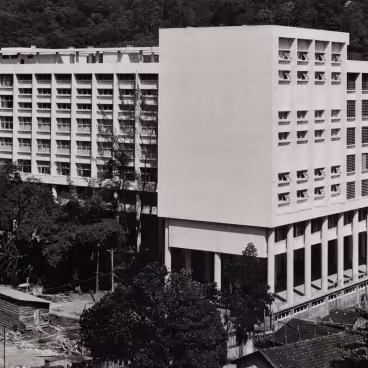 O Edifício da Amizade recém construído. Vê-se na imagem um barracão, restos da obra e também telhados das casas remanescentes da antiga Vila Operária e do Parque Proletário. 1965. Fotógrafo desconhecido. Acervo do Núcleo de Memória da PUC-Rio.