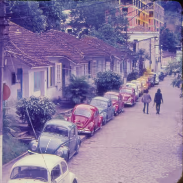 Fuscas enfileirados estacionados na frente das casas da Vila dos Diretórios. 1980c. Fotógrafo desconhecido. Acervo Núcleo de Memória da PUC-Rio.
